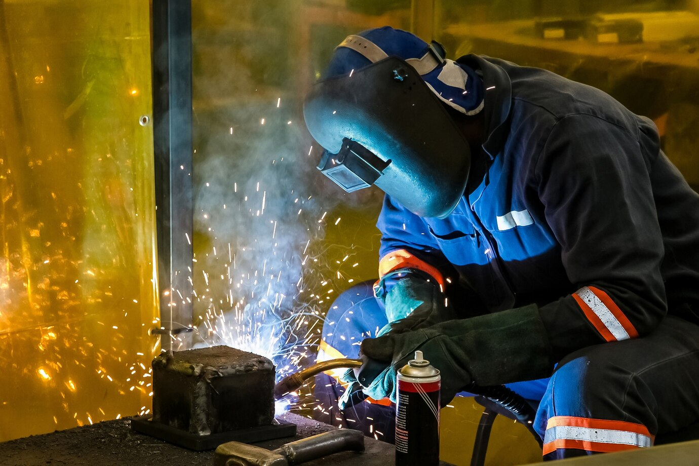 Welder in protective gear sparks bright blue welding light.